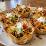 Crispy taco cupcakes filled with ground beef, melted cheddar, lettuce, tomatoes, and sour cream on a white plate.