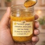 Golden turmeric, ginger, cinnamon, lemon and honey mixture in a glass jar with a spoon lifted above it.