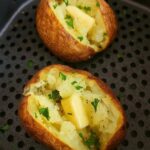 Crispy air fryer baked potatoes split open with fluffy centers, butter, sour cream, and chopped chives.