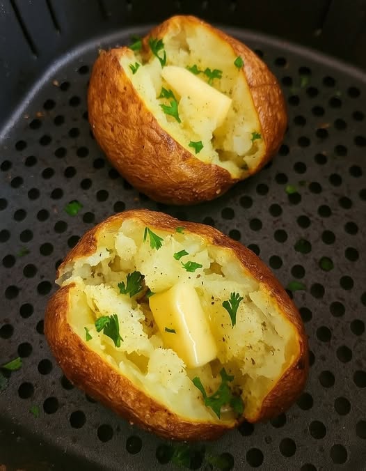 Crispy air fryer baked potatoes split open with fluffy centers, butter, sour cream, and chopped chives.