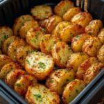 Golden garlic herb baby potato halves with browned edges and chopped parsley in a black air fryer basket.