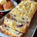 Sliced cream cheese cranberry loaf with red cranberries and a drizzle of vanilla glaze.