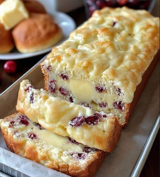 Sliced cream cheese cranberry loaf with red cranberries and a drizzle of vanilla glaze.