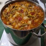 Bowl of vegetable beef soup with tender beef, potatoes, carrots, green beans, corn, and peas in tomato broth.