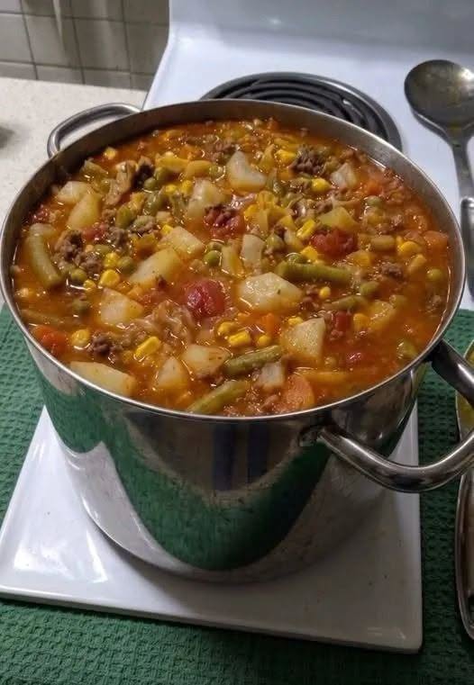 Bowl of vegetable beef soup with tender beef, potatoes, carrots, green beans, corn, and peas in tomato broth.